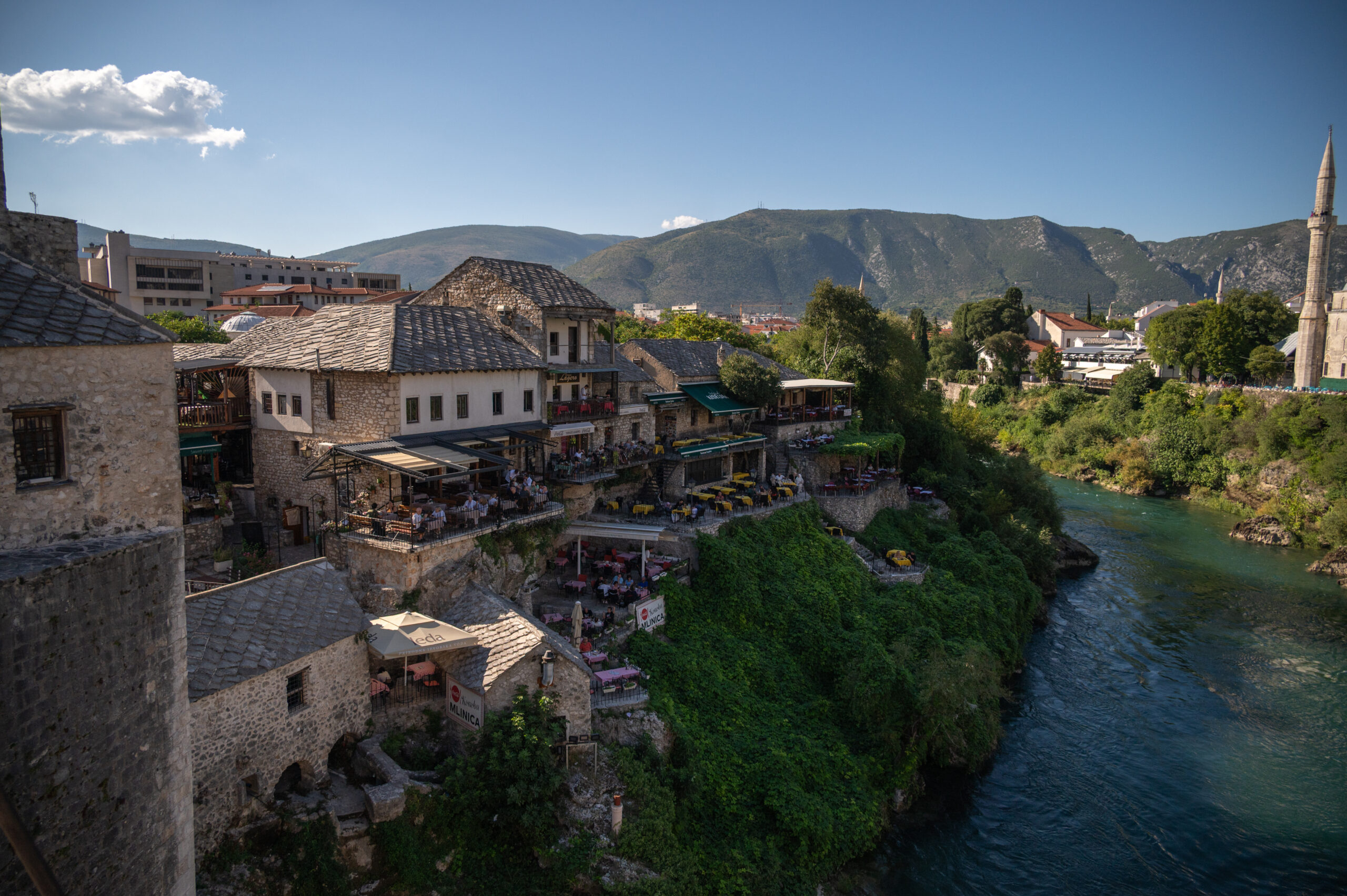 Mostar - wat te doen? Uitzicht vanaf stari most op de rivier in Mostar. Oude ottomaanse gebouwen met op de achtergrond de heuvels.